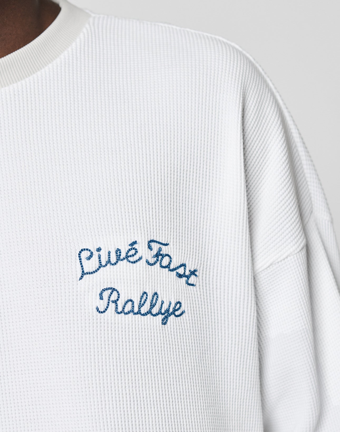 Close-up of the LÉquipe Waffle Longsleeve by LIVE FAST DIE YOUNG: a white textured oversized shirt with blue Live Fast Rallye embroidery on the chest.