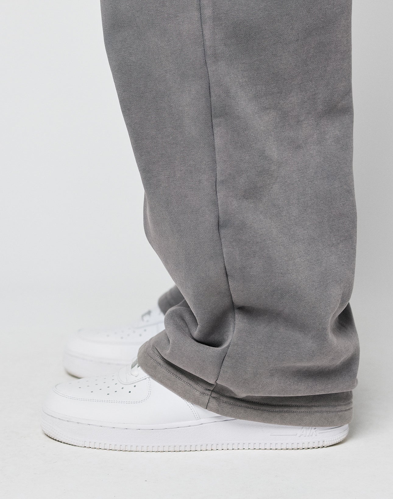 Someone stands against a plain light background wearing LIVE FAST DIE YOUNGs Basic Wide Jogger—loose-fitting gray pants with an elastic waistband and drawstring—that cover the tops of white sneakers.