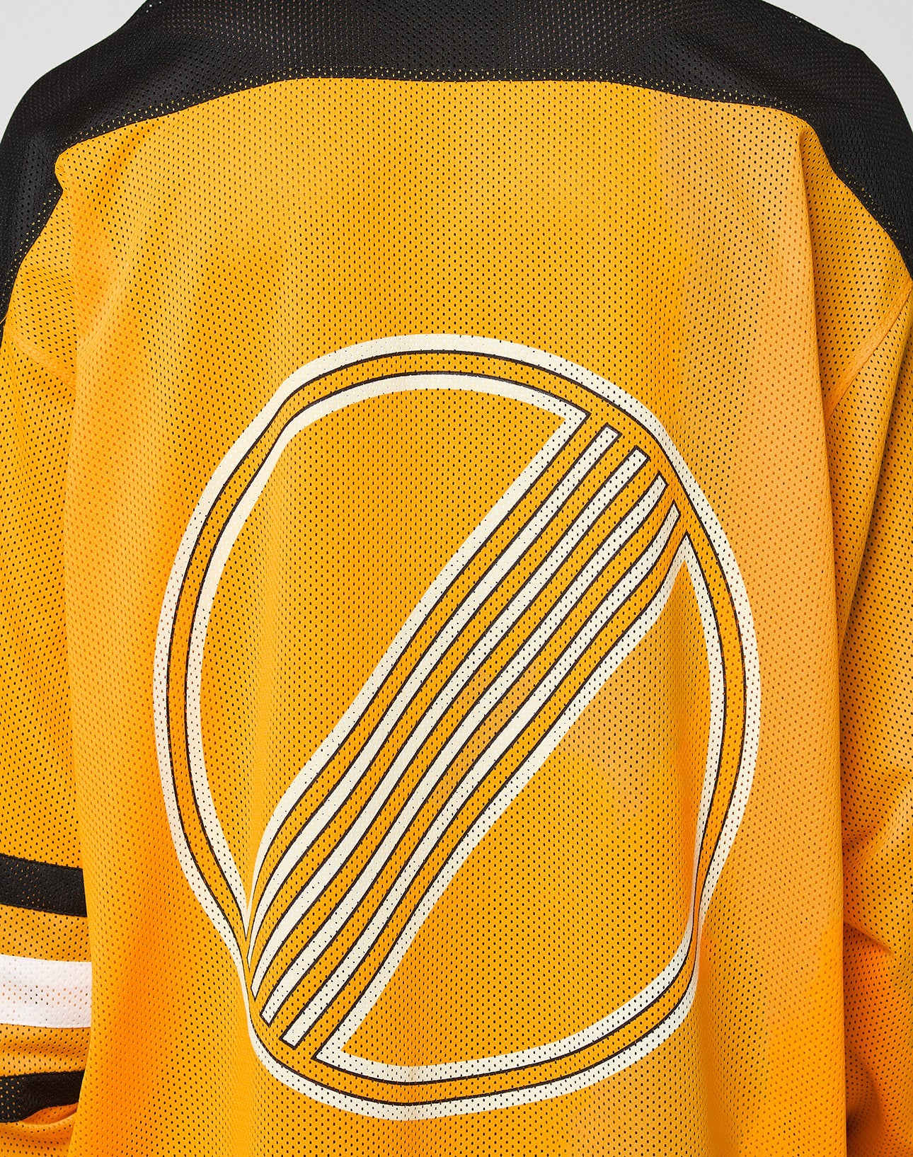 Someone wears the LFDY Autobahn Jersey by LIVE FAST DIE YOUNG—an oversized yellow mesh polyester sports top with black shoulders, striped sleeves, and a large circular white and black multilogo graphic on the back.