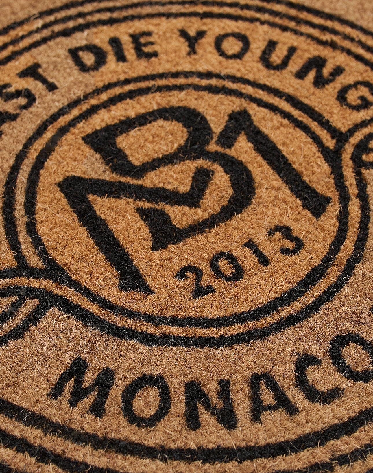 Close-up of the Monaco Boys Doormat by LIVE FAST DIE YOUNG: brown coir mat with black print featuring overlapping MST letters, 2013 and MONACO at the edge. Suitable for indoor and outdoor use.
