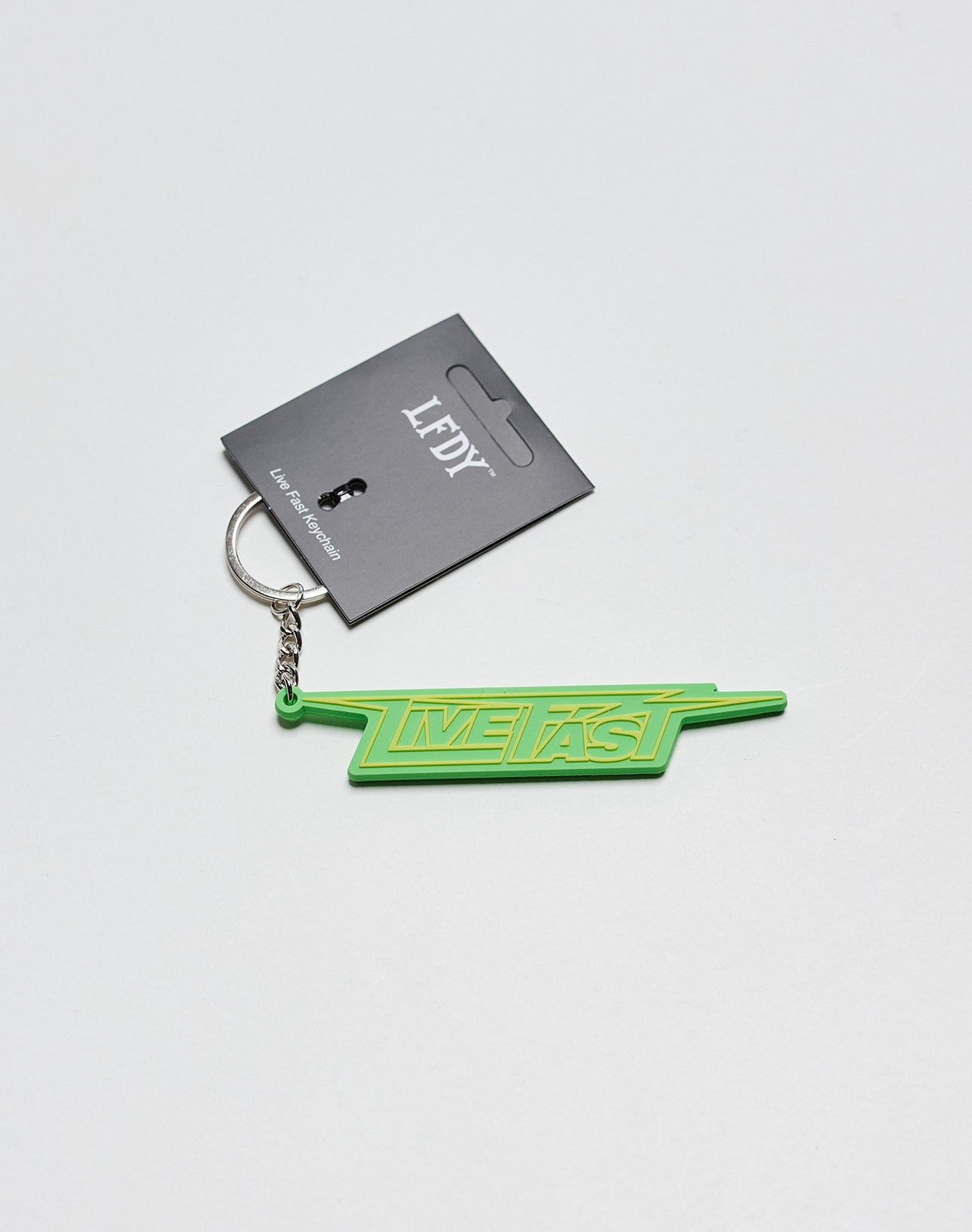 The Live Fast Keychain by LIVE FAST DIE YOUNG is a green silicone keychain with LIVE FAST in bold, a silver ring, and a black LFYT tag featuring a small person silhouette.