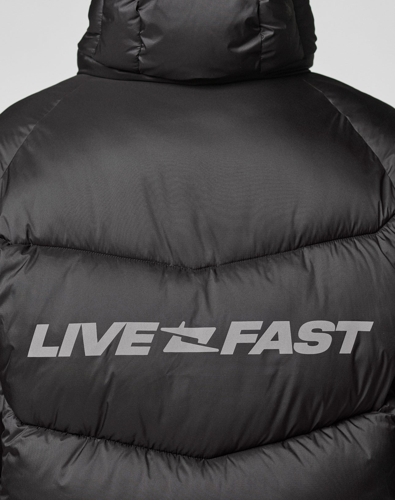 Close-up of the Live Fast Puffer Jacket by LIVE FAST DIE YOUNG: bold, silver LIVE FAST and speed mark printed on the upper back. The oversize fit and reflective print make it both striking and practical.