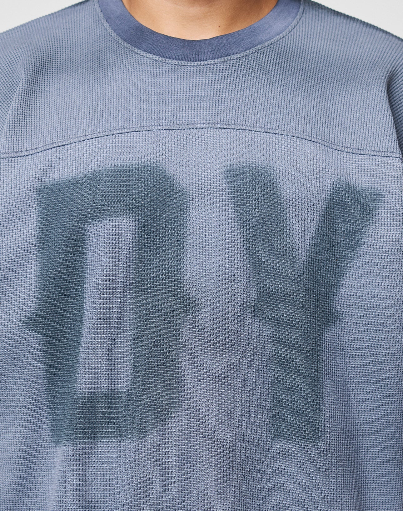 Close-up of a person wearing the LIVE FAST DIE YOUNG Faded Waffle Jersey, an oversized, textured blue shirt made from 100% Baumwolle with large blurred DY letters on the faded front; only neck and upper torso are shown.
