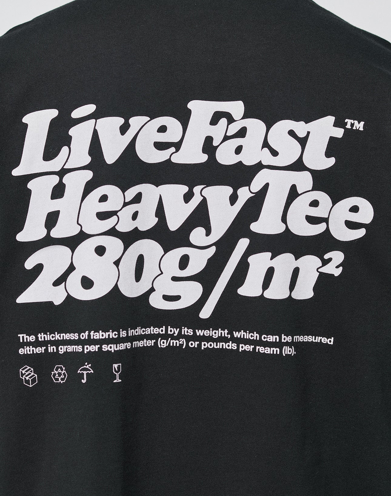 The LIVE FAST DIE YOUNG Basic 280 Tee is a black oversize fit cotton t-shirt with a bold white front print, fabric thickness info in small text, and washing, recycling, and handling icons at the bottom.