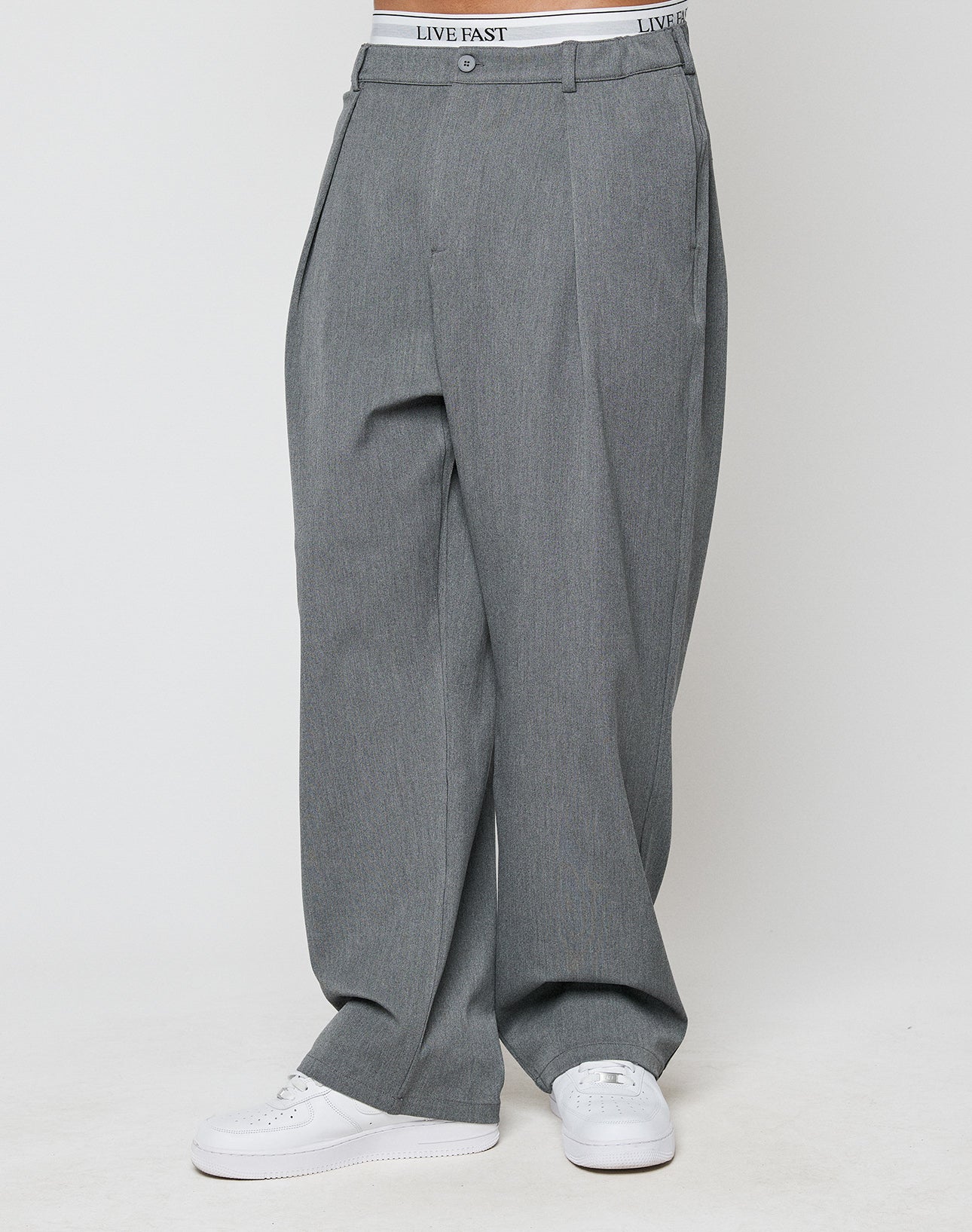 A person wears Wide Casual Pants by LIVE FAST DIE YOUNG—gray, wide fit with a straight leg and elastic waistband—paired with white sneakers, standing against a plain white background.