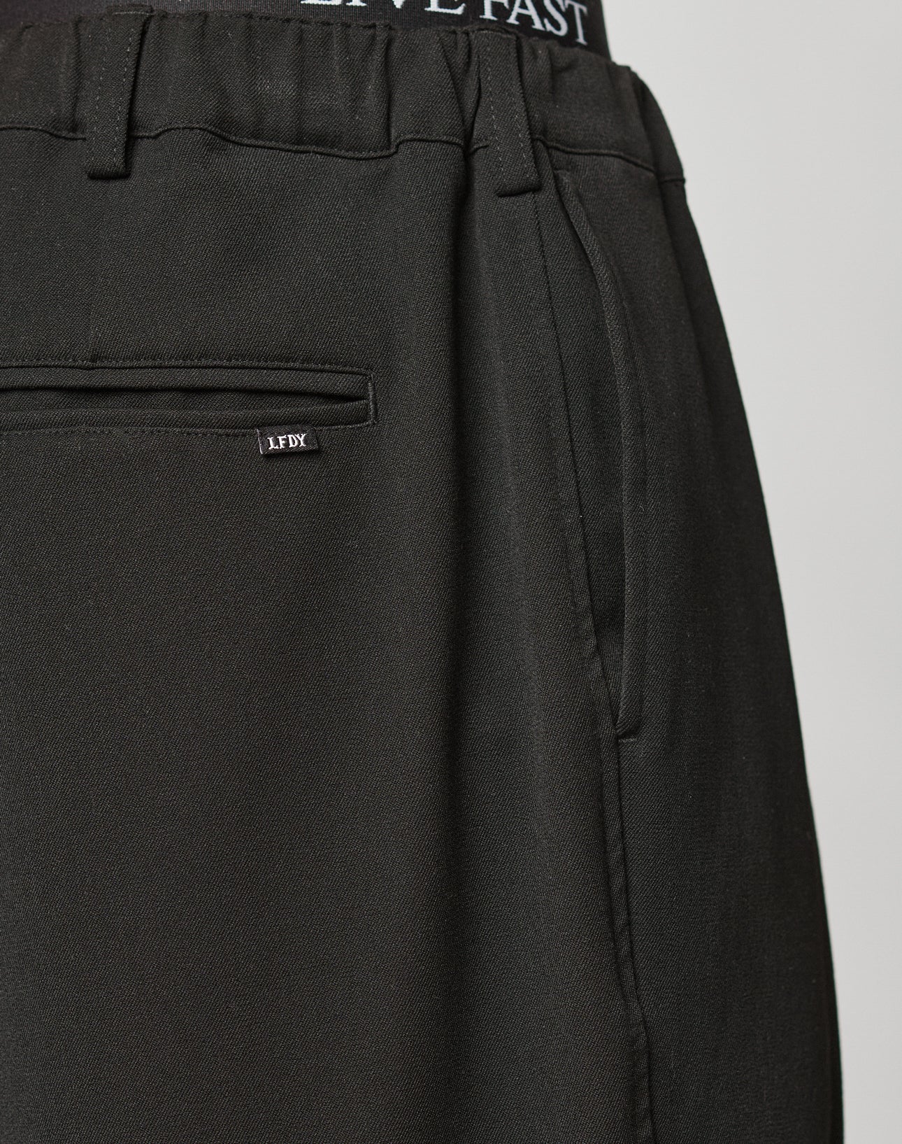 Close-up of Wide Casual Pants by LIVE FAST DIE YOUNG with side pockets, a back pocket featuring a small LFDY label, and an elastic waistband showing LIVE FAST text. Wide Fit offers relaxed comfort and modern style.