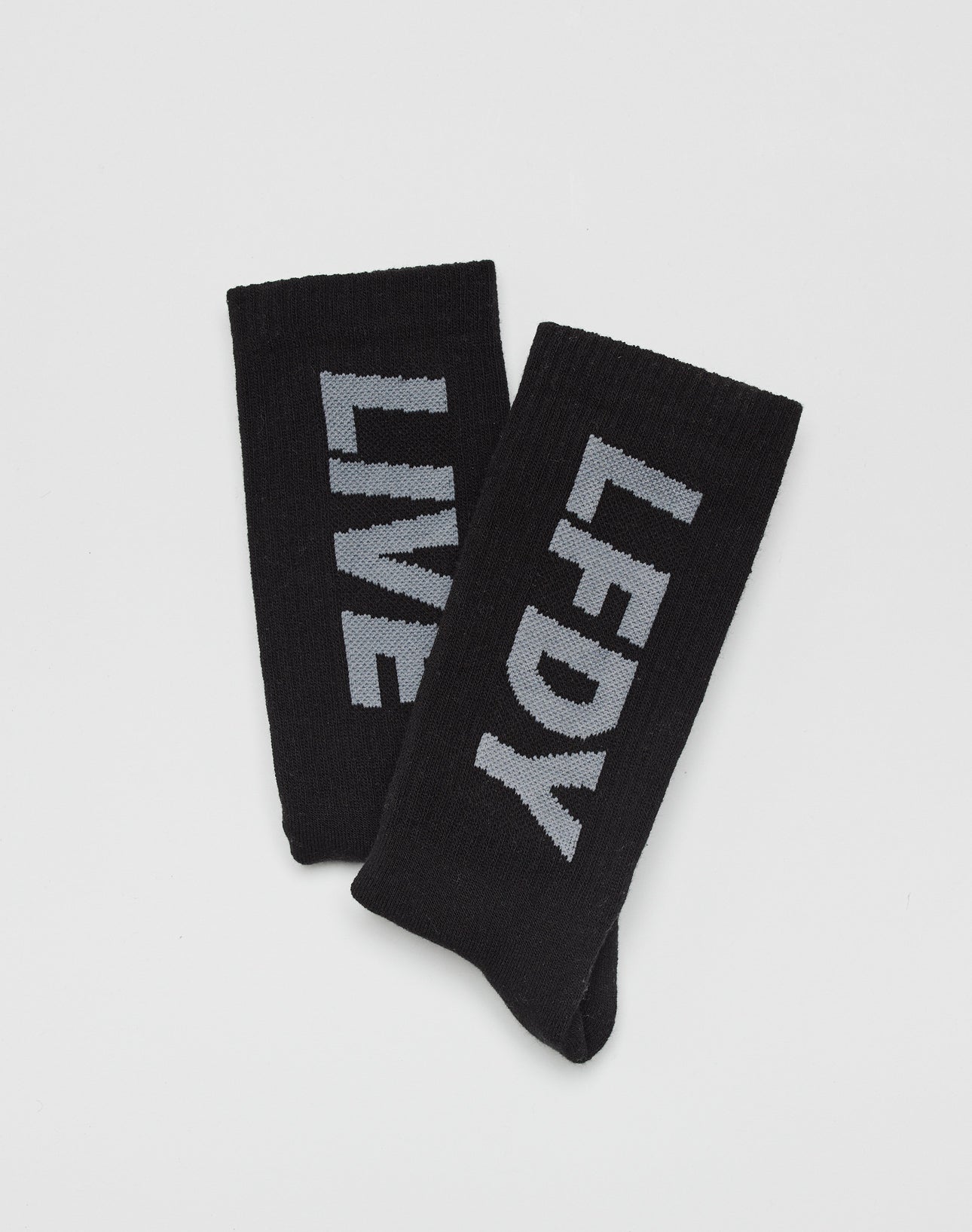 The LIVE FAST DIE YOUNG Basic Typo Socks (2 Pack) features two black cotton socks with bold gray logo text—one reads LFDY, the other LIVE—displayed on a plain white background.