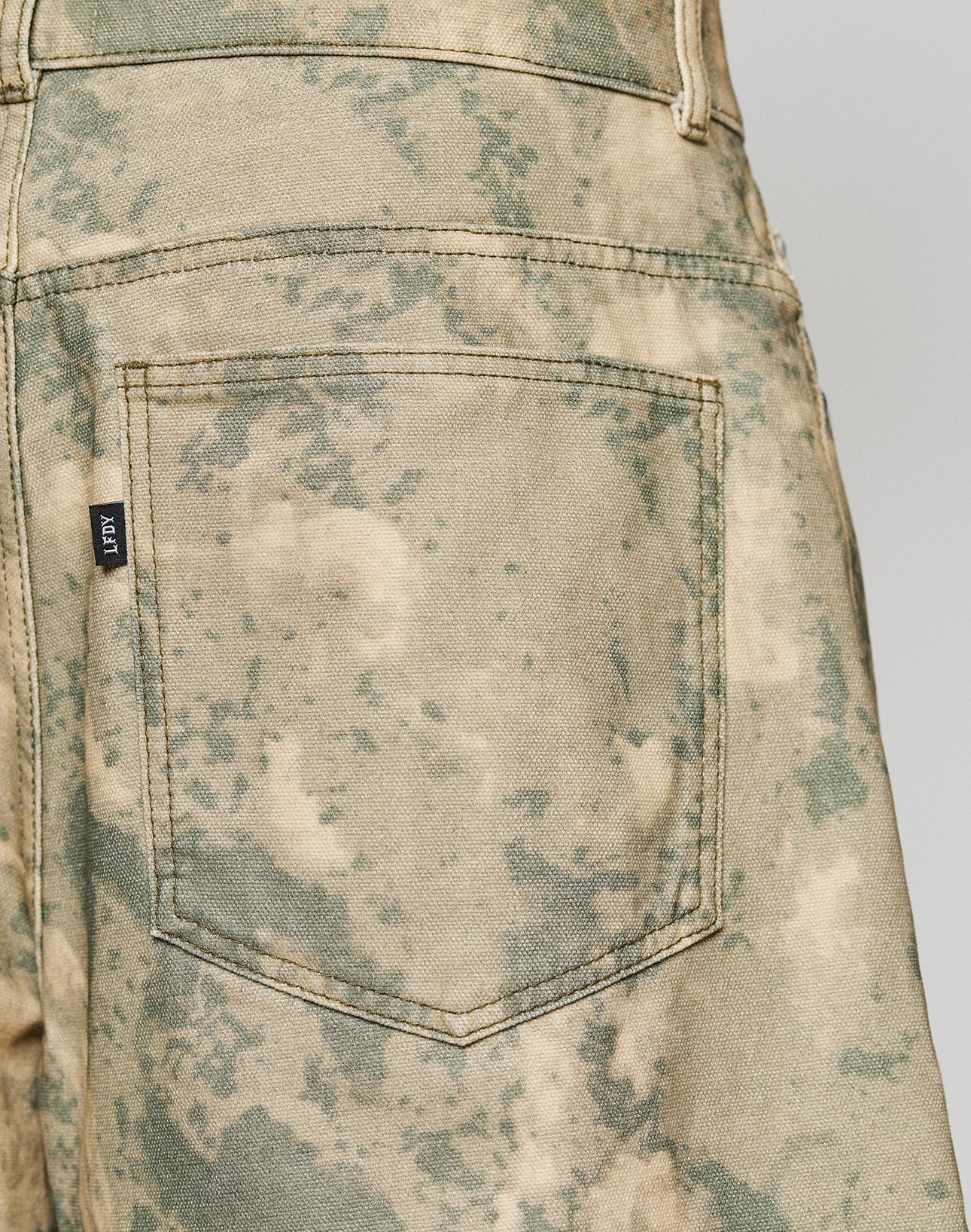Close-up of the back pocket on LIVE FAST DIE YOUNG Canvas Shorts. Features visible stitching, a baggy fit, a small black tag on the pocket, and is made from 100% cotton.