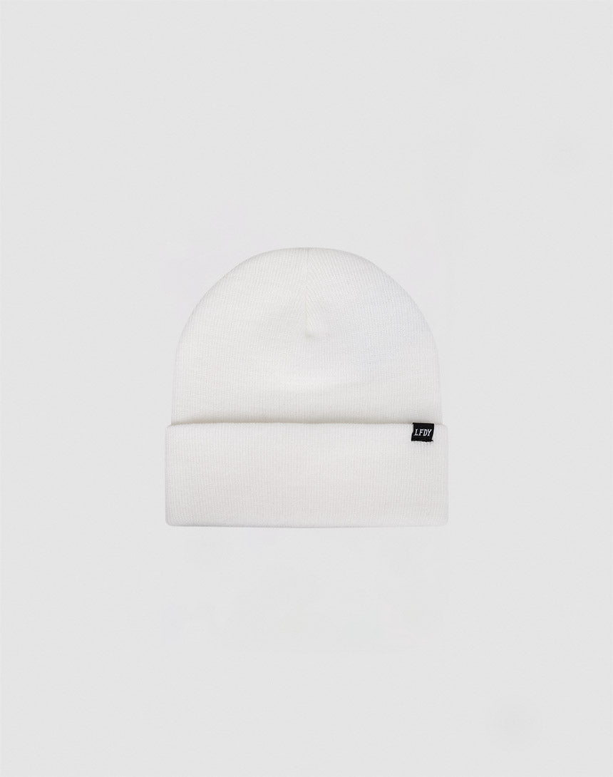 The Basic Beanie by LIVE FAST DIE YOUNG is a plain white polyacryl knit with a folded cuff and a small black front tag. Light grey background. Handwäsche recommended for lasting quality.