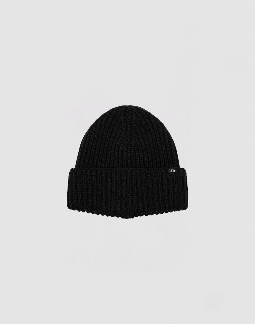 A black Rib Knit Beanie by LIVE FAST DIE YOUNG, made from soft Polyacryl with a folded brim, is centered on a plain light gray background.