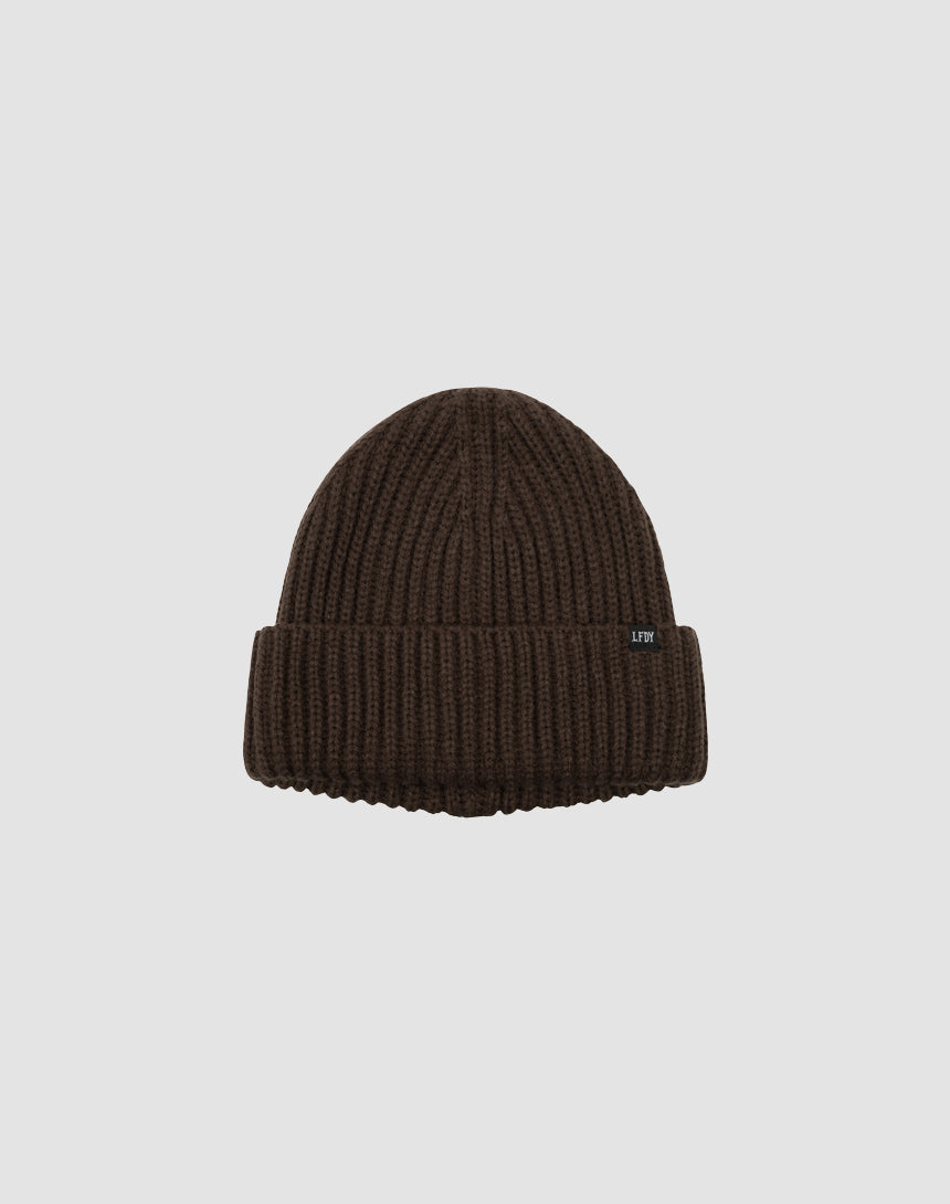 A brown LIVE FAST DIE YOUNG Rib Knit Beanie with a folded brim and small black side flaglabel, shown on a plain light gray background.
