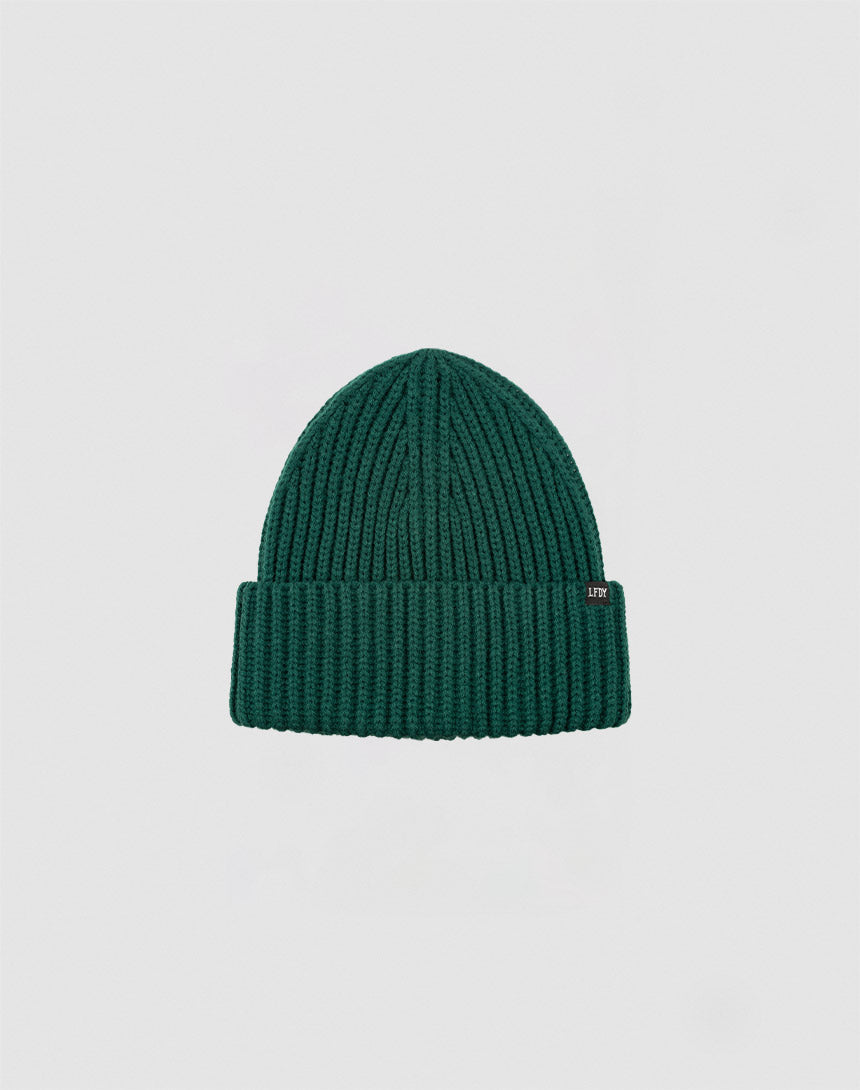 A LIVE FAST DIE YOUNG Rib Knit Beanie in green, featuring a folded brim with a small rectangular flag label, is centered on a plain light gray background.