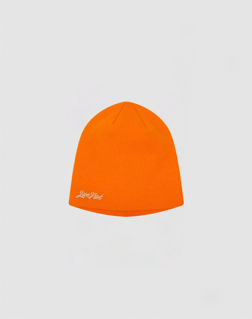 The Script Beanie by LIVE FAST DIE YOUNG is a bright orange polyacryl hat featuring a small white Just Don logo stitch on the lower left side, shown against a plain light gray background.
