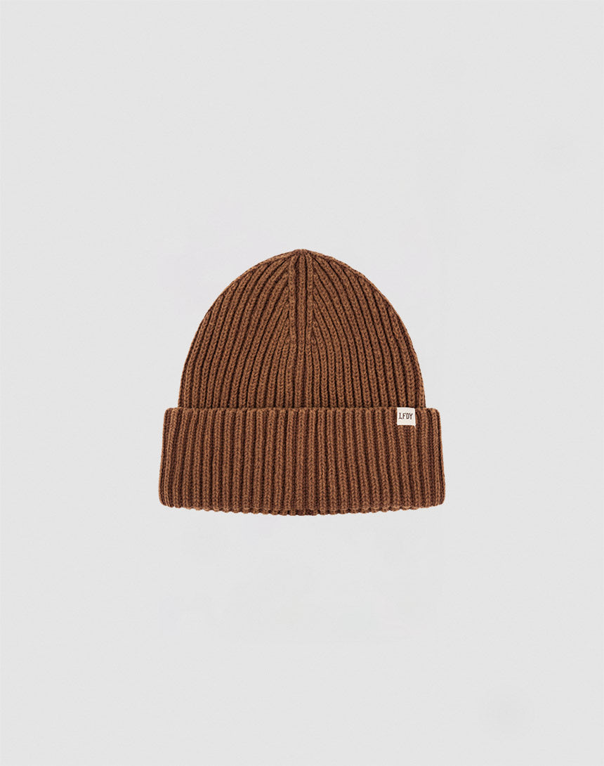 The LIVE FAST DIE YOUNG Washed Rib Knit Beanie in brown cotton features a folded cuff and a small white rectangular side tag, shown against a plain light gray background.