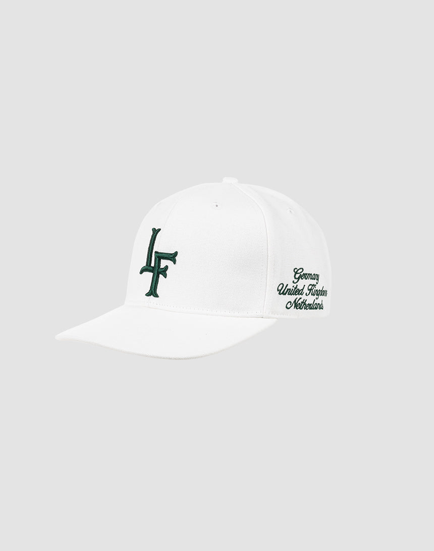 The LF Snapback by LIVE FAST DIE YOUNG is a white cotton baseball cap with a dark green LF logo on the front and Germany United Kingdom Netherlands in script on the left side. Features snap closure. Shown on a light gray background.