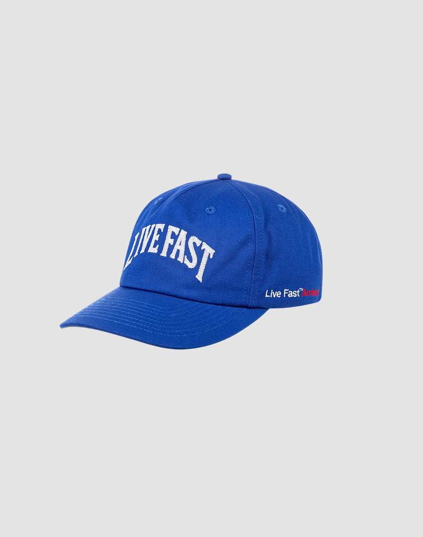 The LIVE FAST DIE YOUNG Live Fast Unstructured Cap is royal blue with LIVE FAST in large white embroidery on the front, a Flag-Label on the side, and an adjustable closure. Displayed on a light gray background.