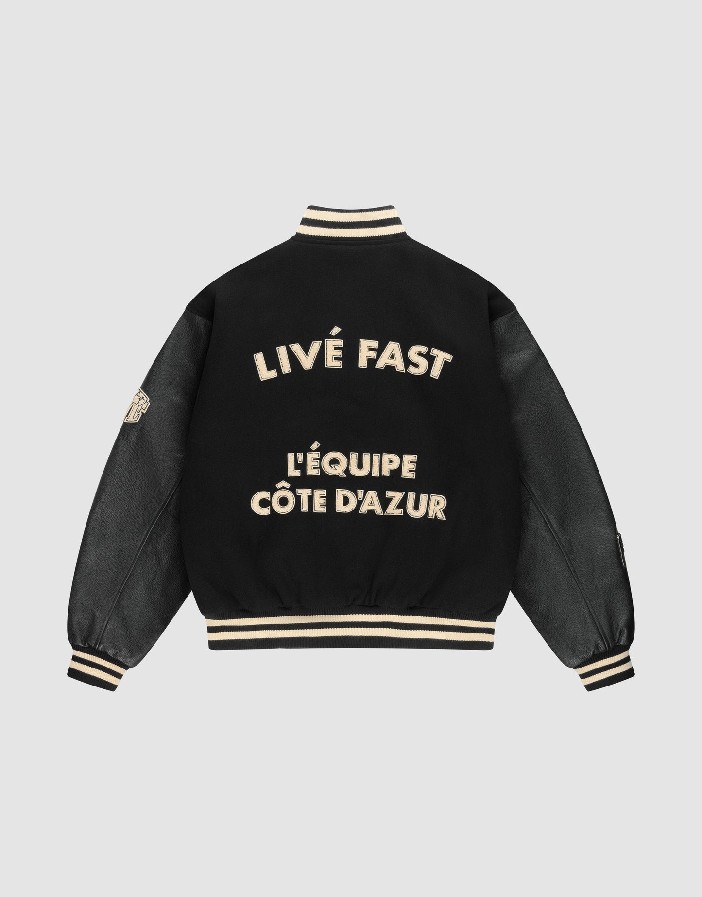 The LFDY x Schott NYC Varsity Jacket by LIVE FAST DIE YOUNG is a limited edition black jacket with cream trim and leather sleeves, featuring bold cream "LIVE FAST" and "LÉQUIPE CÔTE DAZUR" text on the back plus a left sleeve patch.