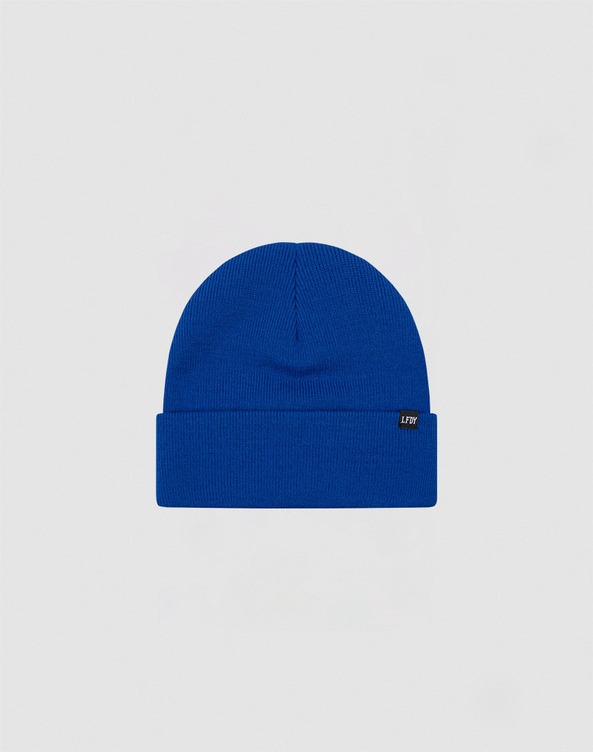 The LIVE FAST DIE YOUNG Basic Beanie is a plain royal blue polyacryl hat with a folded brim and a small black side flag label with white text, shown on a light gray background.