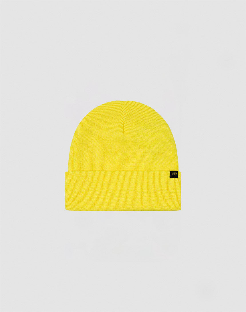 The LIVE FAST DIE YOUNG Basic Beanie is a bright yellow Polyacryl knit hat with a folded brim and small black flaglabel on the left, shown against a plain light gray background. One size for versatile comfort.