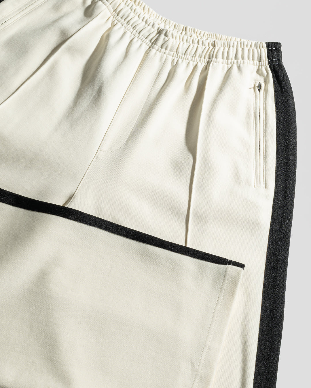 The LIVE FAST DIE YOUNG LFDY Striped Jogger features a cream color with black side panels and trim, an elastic waistband, multiple pockets including a large leg pocket, and stylish chevron tape detailing.