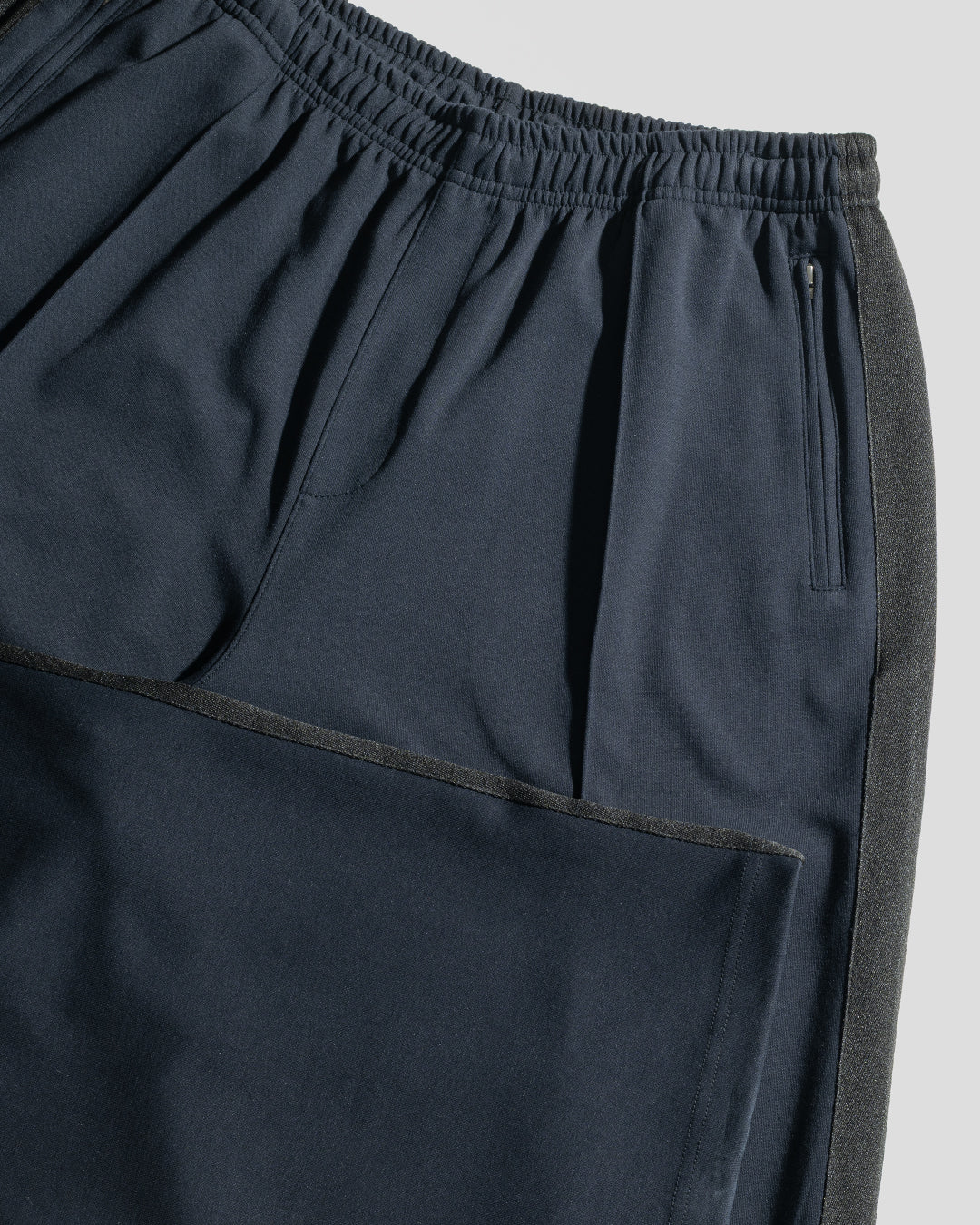 Close-up of the LFDY Striped Jogger by LIVE FAST DIE YOUNG in navy blue with elastic waistband, side zipper pocket, and dark gray side panels, laid flat on a light gray background.