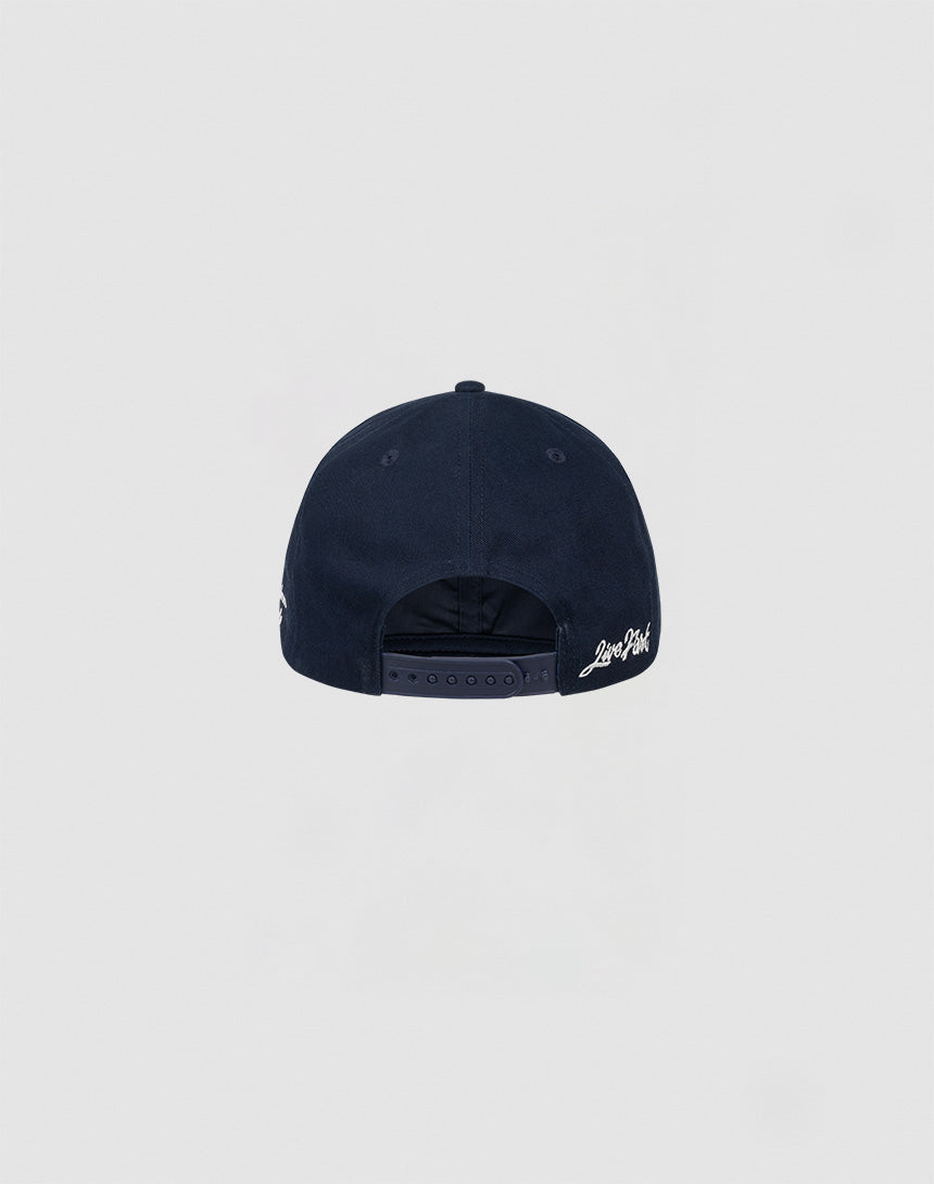 The LF Snapback by LIVE FAST DIE YOUNG is a navy blue cotton baseball cap. Shown from the back, it features an adjustable snap closure and white LIVE FAST DIE YOUNG logo stitching on the left near the closure. Background: plain light gray.