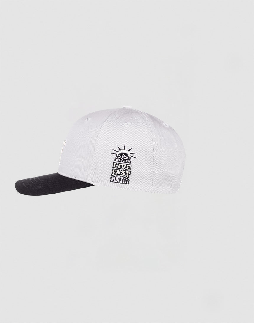 The LF Snapback by LIVE FAST DIE YOUNG is a white cap with a black brim and black underside, featuring an embroidered Statue of Liberty patch and LOCAL LEGEND HAVE EAST MANTH text. It has a snap closure for a perfect fit. Light gray background.