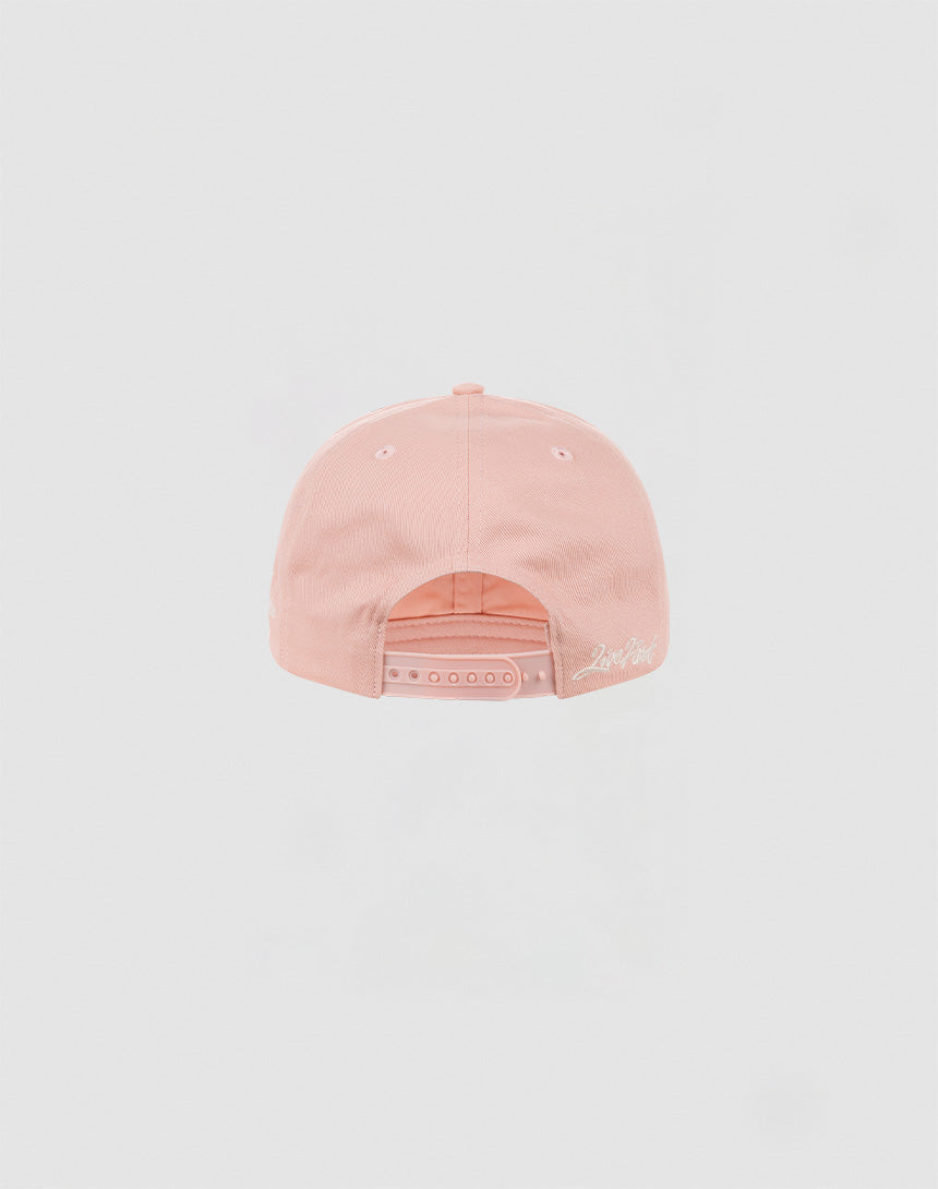 The LF Snapback by LIVE FAST DIE YOUNG is a light pink cotton baseball cap, shown from the back with a snap closure and white embroidered logo in script near the edge.