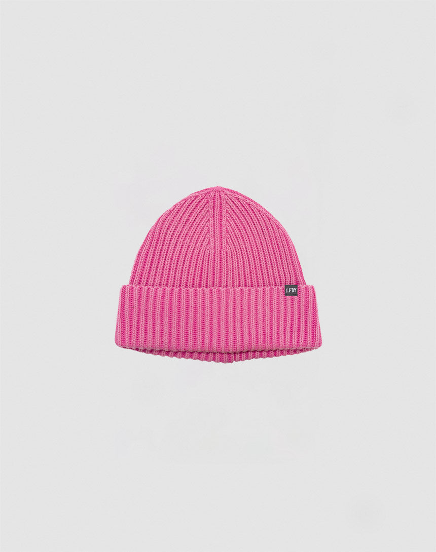 A bright pink Washed Rib Knit Beanie by LIVE FAST DIE YOUNG, made of cotton with a folded brim and a small black rectangular tag on the side, displayed against a plain light background.