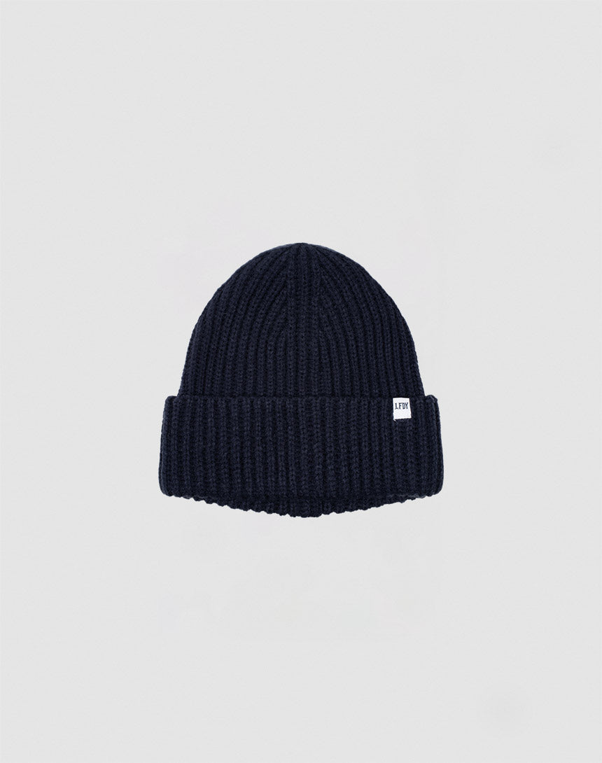 The LIVE FAST DIE YOUNG Rib Knit Beanie in navy blue, made from soft polyacryl with a folded brim and small white side tag, is shown on a plain light gray background.
