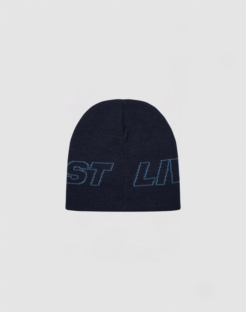 The Live Fast Jacquard Beanie by LIVE FAST DIE YOUNG is a dark navy polyacryl knit hat with light blue outlined “Logo Strick Outline” text wrapping around it, shown against a plain light gray background.