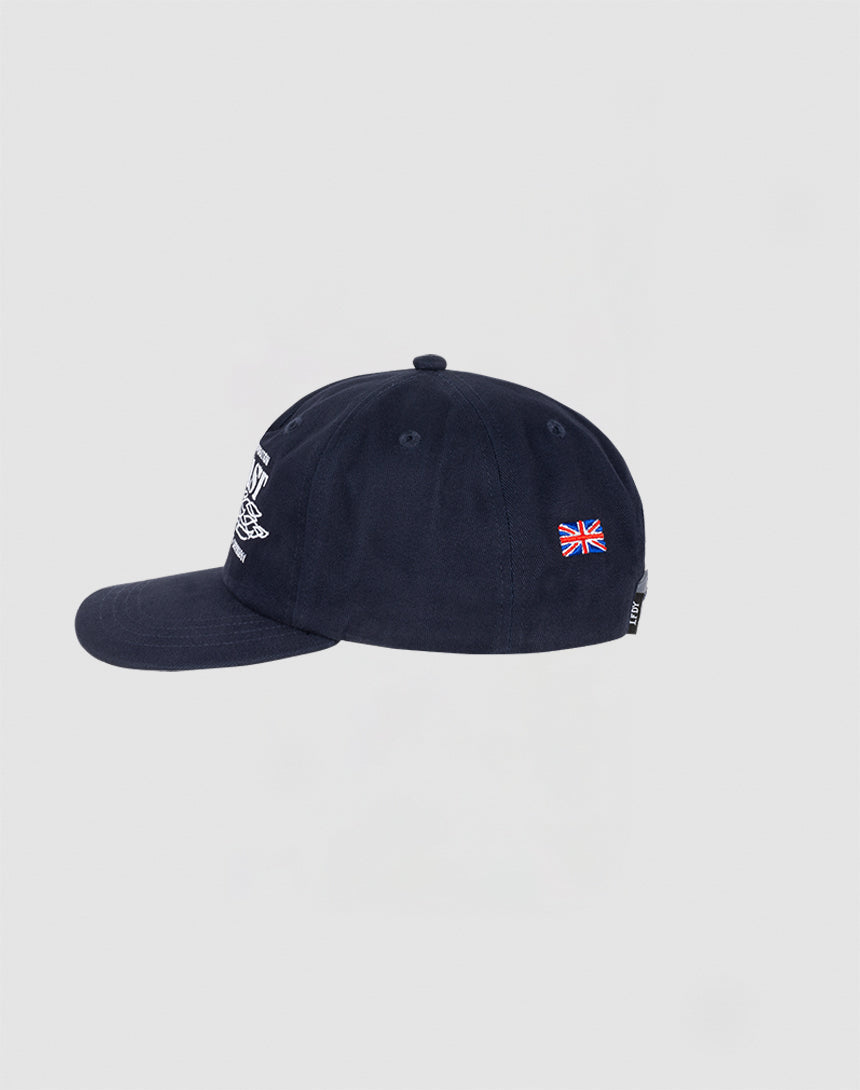 The Live Fast Corporation Cap by LIVE FAST DIE YOUNG is shown from the side in navy blue, with a small embroidered British flag Stick Flag-Label on the back, white front stitching, and a plain light gray background.