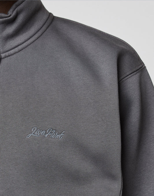 Close-up of a person wearing a grey LIVE FAST DIE YOUNG Sweatsuit Jacket with a standing collar and "Live First" embroidered on the chest in grey thread.