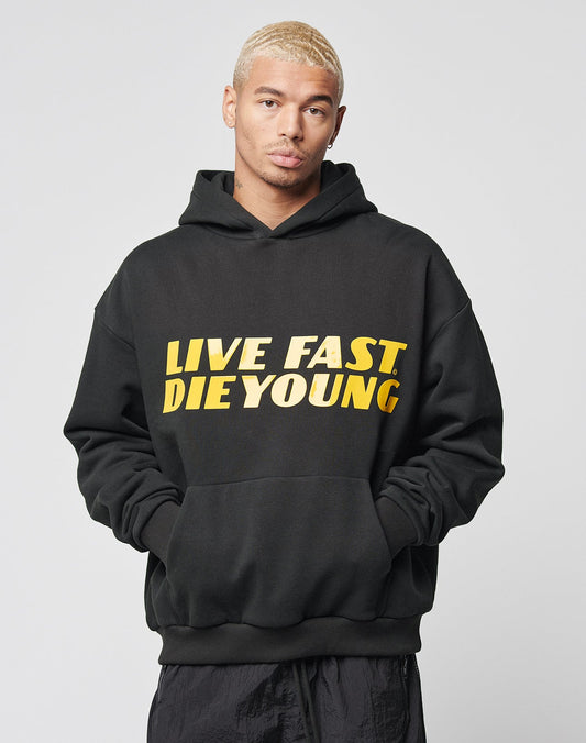 A person with short blond hair wears the LIVE FAST DIE YOUNG LFDY Drift Hooded, standing against a plain light background and looking directly at the camera with hands in pockets.