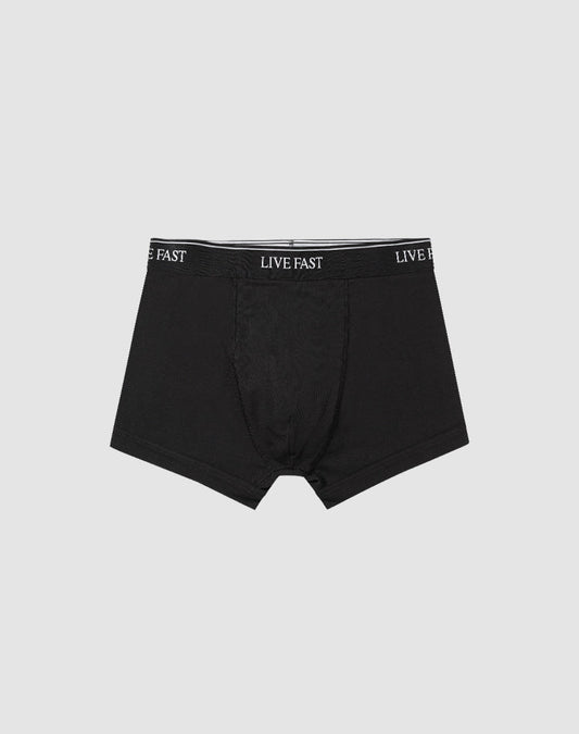A pair of black Live Fast Trunks (2 Pack) by LIVE FAST DIE YOUNG, made from soft cotton with LIVE FAST repeatedly printed in white on the elastic waistband, displayed on a plain light gray background.