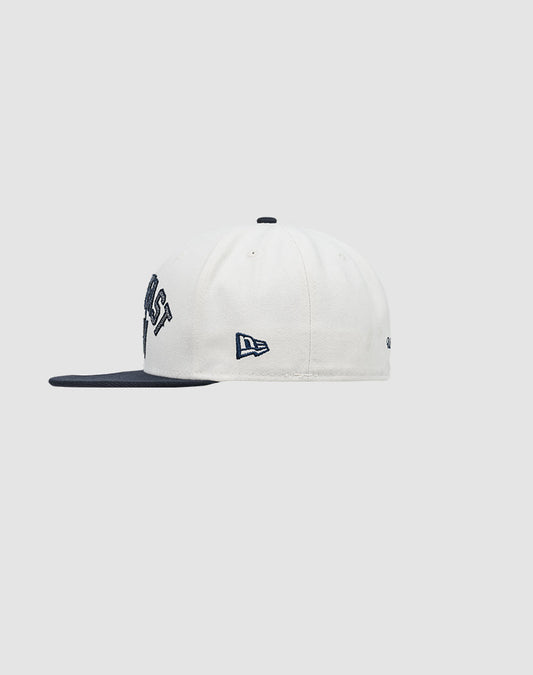 The LFDY X NEW ERA 59FIFTY Fitted Cap by LIVE FAST DIE YOUNG features a white crown, dark navy visor, and navy embroidery including the New Era logo. Shot from the side against a light gray background. Größentabelle available for fit.