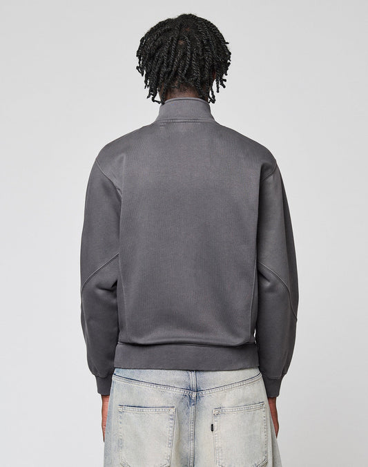 A person with medium-length, twisted hair is seen from behind in a gray LIVE FAST DIE YOUNG Sweatsuit Jacket and light-washed jeans, standing against a plain light gray background.