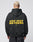 A person with short blond hair wears the LFDY Drift Hooded by LIVE FAST DIE YOUNG, a black hoodie with yellow LIVE FAST. DIE YOUNG text on the back, Oversize Fit, and doppellagige Kapuze, against a plain light background.