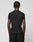 A person with short, twisted hair is shown from behind in a plain black LIVE FAST DIE YOUNG LFDY Slim Tee and black pants against a light gray background. A small Flag-Label detail completes the minimalist look.
