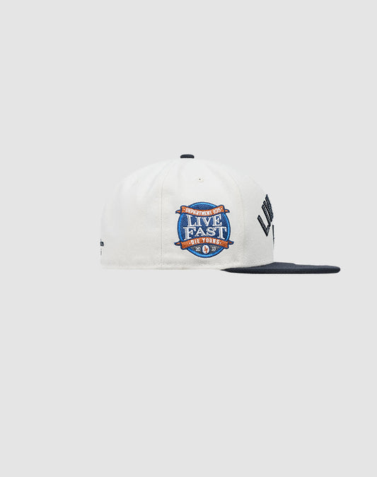 The LIVE FAST DIE YOUNG x NEW ERA 59FIFTY fitted cap in white and navy features a side-embroidered LFDY patch, shown on a plain gray background. Check the Größentabelle for perfect sizing.