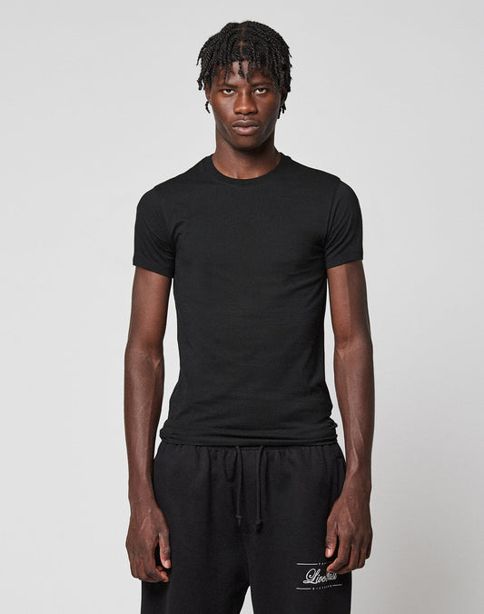 A young man with short, twisted hair wears the LFDY Slim Tee from LIVE FAST DIE YOUNG and black sweatpants, standing against a light gray background with a neutral expression. | model