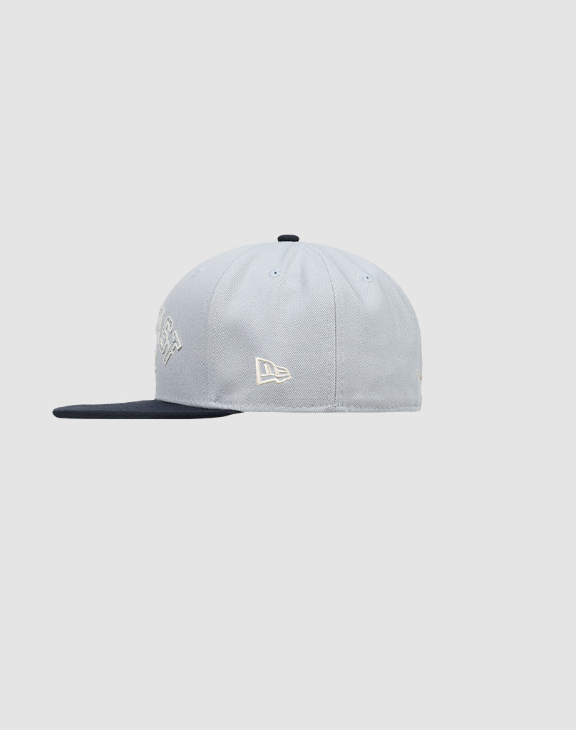 The LFDY X NEW ERA 59FIFTY by LIVE FAST DIE YOUNG is a light gray fitted cap with a black brim, shown side view on a light gray background. Features a small white embroidered logo on the side. Größentabelle available for perfect fit.