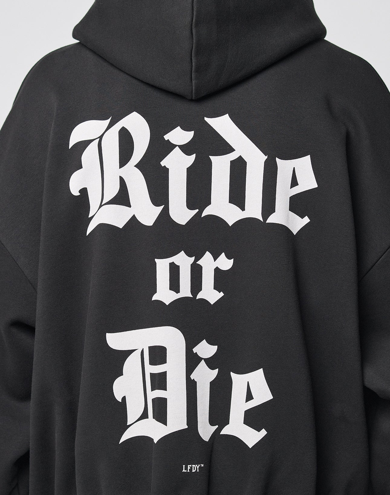A person wearing the LIVE FAST DIE YOUNG Ride or Die Hooded Zip, a black hoodie with bold white Gothic-style Ride or Die text on the back, featuring an oversize fit and doppellagige Kapuze for comfort.