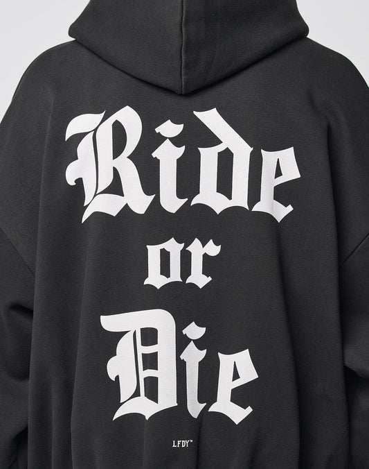 A person wearing the LIVE FAST DIE YOUNG Ride or Die Hooded Zip, a black hoodie with bold white Gothic-style Ride or Die text on the back, featuring an oversize fit and doppellagige Kapuze for comfort.