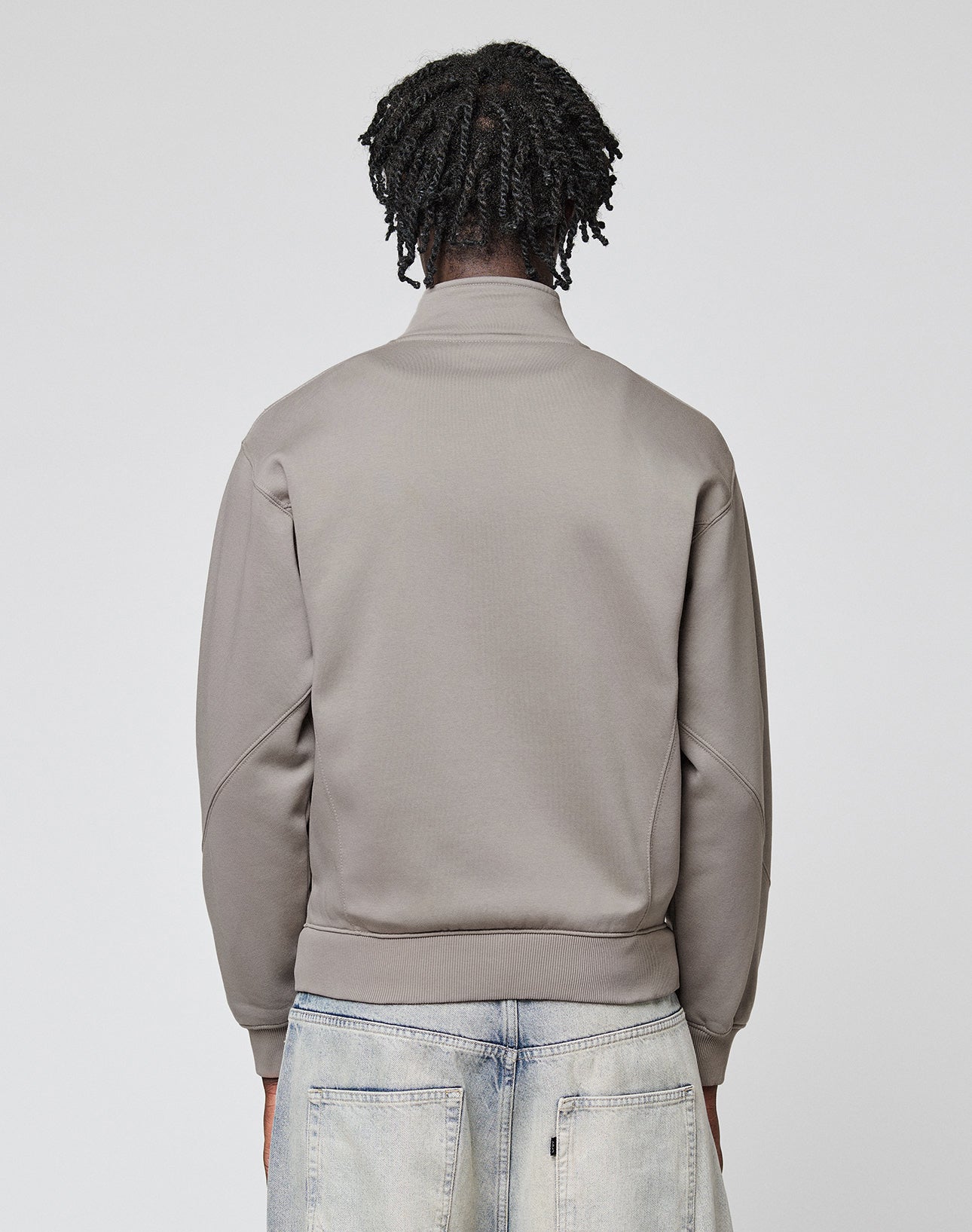 A person with short, twisted hair is shown from the back wearing a LIVE FAST DIE YOUNG Sweatsuit Jacket with Stehkragen and faded blue Regular Fit jeans, against a plain light gray background.