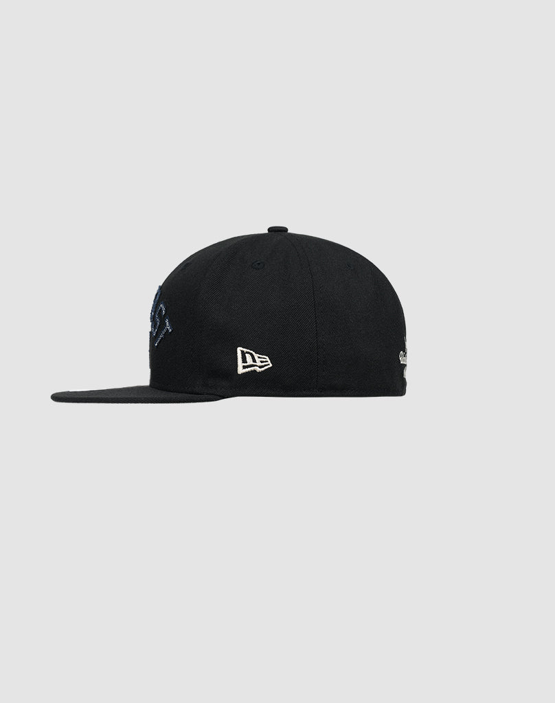 A black LFDY X NEW ERA 59FIFTY fitted cap by LIVE FAST DIE YOUNG, shown from the side with a white embroidered New Era logo on the side panel, set against a plain light gray background. Check Größentabelle for sizing.