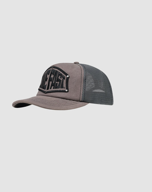 The LFDY Rivet Trucker by LIVE FAST DIE YOUNG is a gray and black mesh cap with “LIVE FAST” embroidered on the front and a subtle flag-label detail, shown against a plain light gray background.| model 
