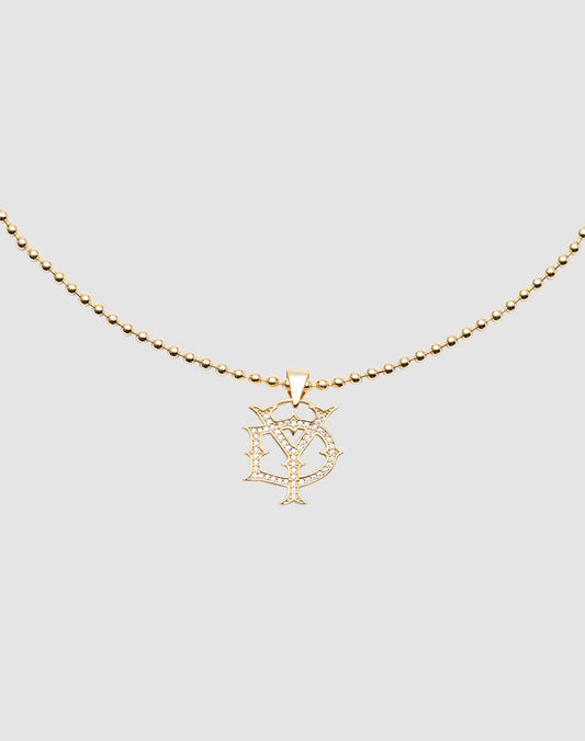 The DY Chain by LIVE FAST DIE YOUNG is a gold-plated beaded necklace with a cubic zirconia pendant featuring stylized overlapping D and Y letters, shown on a plain light gray background.