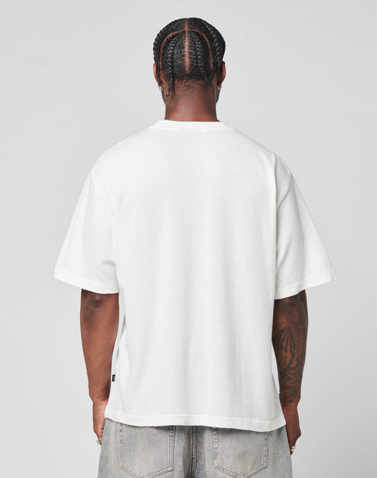 With their back to the camera, a person with braided hair wears the LIVE FAST DIE YOUNG LFDY Vintage Tee in plain white and light blue jeans against a simple, light gray background.