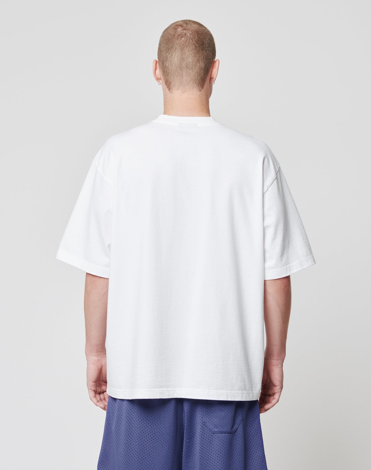 A person with short hair, seen from the back, wears a LIVE FAST DIE YOUNG Basic Tee in plain white and blue mesh shorts against a light gray background.